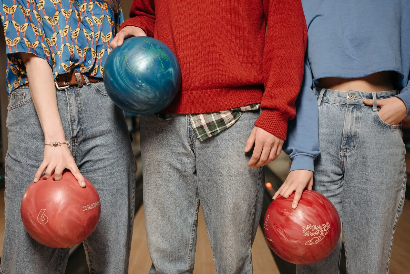 A group of three friends casually holding bowling balls at an indoor alley, ready to play.